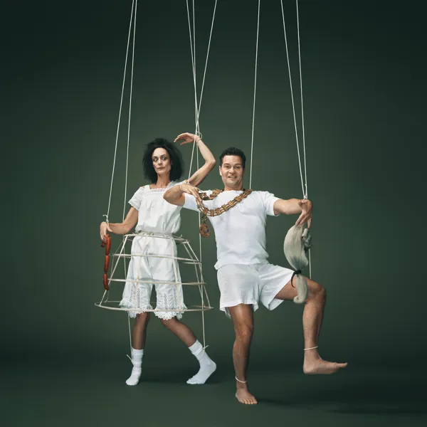 En kvinde og mand i gammeldags hvidt undertøj. Hun i krinoline og holder pølseranke. Han med borgmesterkæde og holder en paryk. Fra forestilling Kandestøberen på Odense Teater.