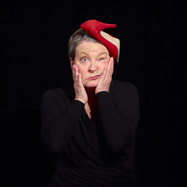 En kvinde i sort med rød stilet på hovedet. Laver en mærkelig ansigtsgrimasse. Fra teaterforestilling Ansigtsyoga for begyndere på Odense Teater